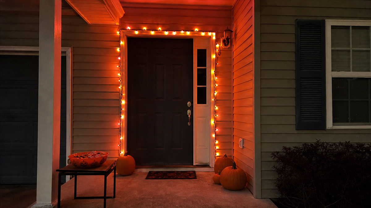 Front door decorated with orange string lights and a bowl of candy, before the rug